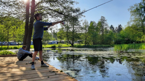 Due persone pescano vicino allo stagno a Skovly Camping, circondati dal verde e tende nella Regione Sjælland.