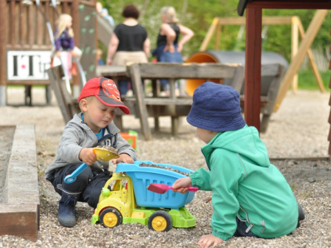 To børn leger sammen med en legetøjslastbil i sandet på en legeplads ved Skovly Camping, Region Sjælland.