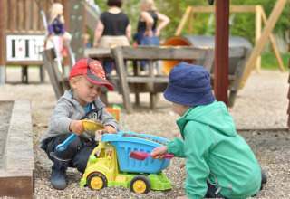 Deux enfants jouent avec un camion-jouet dans le sable à l’aire de jeux de Skovly Camping, région du Sjælland.