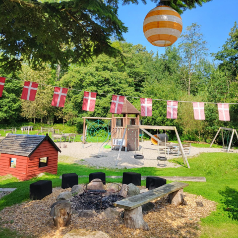 Aire de jeux avec drapeaux danois, coin feu et cabane à Skovly Camping, région Sjælland, Danemark.