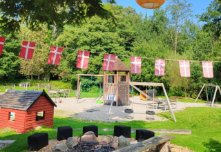 Playground with Danish flags, firepit, playhouse, and play equipment at Skovly Camping, Region Zealand, Denmark.