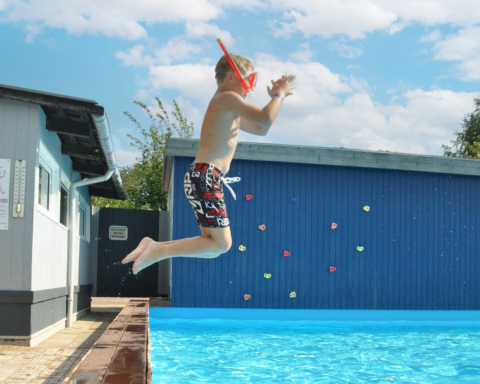 Boy with snorkel jumping into pool at Skovly Camping, Region Zealand, Denmark, on a sunny summer day.