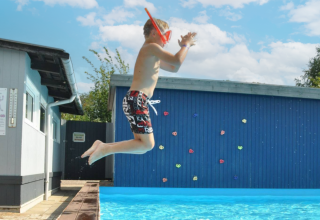 Boy with snorkel jumping into pool at Skovly Camping, Region Zealand, Denmark, on a sunny summer day.