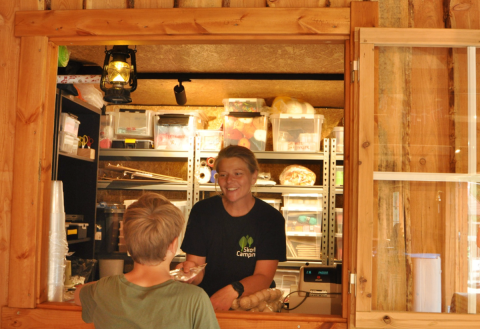 Persona atendiendo a un huésped en el mostrador de madera de Skovly Camping, Región de Selandia, Dinamarca.