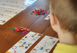 Un bambino gioca a bingo con immagini e gettoni colorati su un tavolo di legno in un campeggio per famiglie.