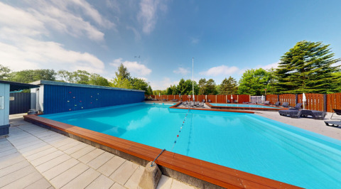Piscina all’aperto a Skovly Camping con lettini, recinzione e alberi nella regione di Zealand, Danimarca.