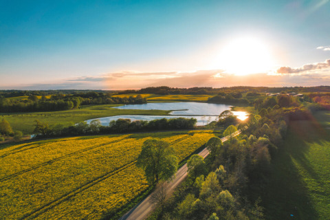 Luftfoto af Skovly Camping i Region Sjælland, Danmark, med solnedgang, sø og grønne marker.
