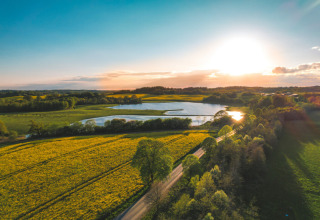Vista aerea di Skovly Camping in Regione Sjælland, Danimarca, al tramonto con campi e lago.