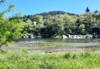 Clear river with green trees and grassy banks at Camping Paradis Family des Issoux in Auvergne-Rhône-Alpes, France.