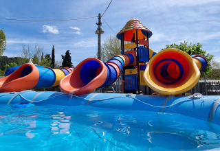Parque acuático con toboganes tubulares coloridos y torre junto a la piscina en Camping Paradis Family des Issoux, Francia.