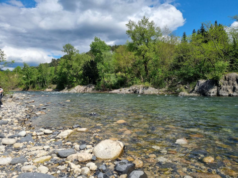 Río y orilla rocosa rodeados de árboles en Camping Paradis Family des Issoux, Auvergne-Rhône-Alpes, Francia.