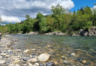 Rivière avec berge rocailleuse et arbres verts au Camping Paradis Family des Issoux, Auvergne-Rhône-Alpes, France.