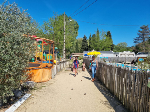 Sendero en Camping Paradis Family des Issoux con área de juegos, visitantes y cielo azul despejado.