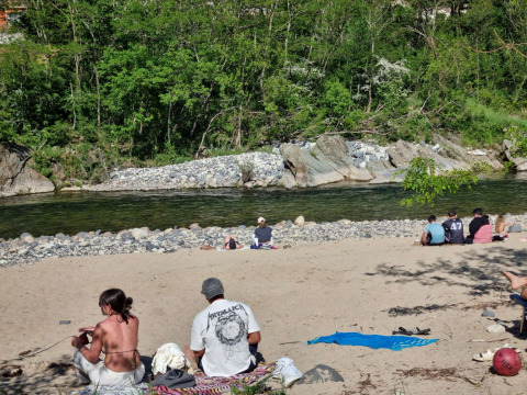 Personas descansando en la orilla arenosa del río en Camping Paradis Family des Issoux, rodeados de naturaleza.