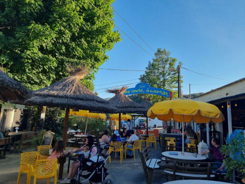 Udendørs caféområde med gule parasoller og stråtage, folk hygger i solen på Camping Paradis Family des Issoux.