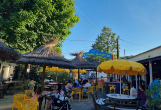 Terraza con sombrillas amarillas en Camping Paradis Family des Issoux, Auvergne-Rhône-Alpes, Francia, con gente sentada.