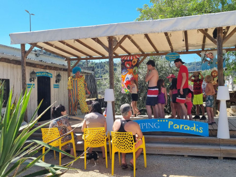 Familien und Kinder nehmen an Aktivitäten auf einer überdachten Bühne mit Clown im Camping Paradis Frankreich teil.