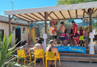 Famiglie e bambini partecipano ad attività con un clown sul palco coperto al Camping Paradis in Francia.