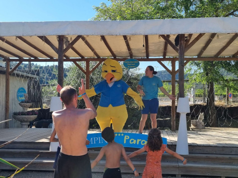 Kinder und Erwachsene tanzen vor einer Bühne mit einem Entenmaskottchen im Camping Paradis Family des Issoux.