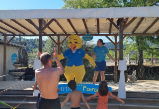 Kinderen en volwassenen dansen voor een podium met een eendenmascotte in Camping Paradis Family des Issoux, Frankrijk.