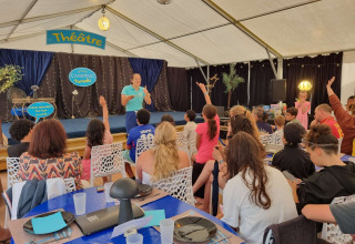 Kinder und Erwachsene nehmen an einer Veranstaltung im Theaterbereich des Camping Paradis Family des Issoux teil.