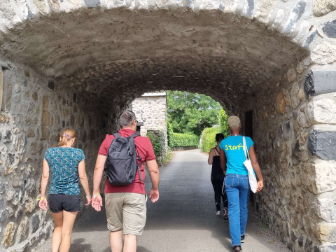 Quattro persone camminano sotto un arco di pietra al Camping Paradis Family des Issoux in Auvergne-Rhône-Alpes, Francia.