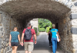 Fire personer går under en stenmuret tunnel i Camping Paradis Family des Issoux i Auvergne-Rhône-Alpes, Frankrig.