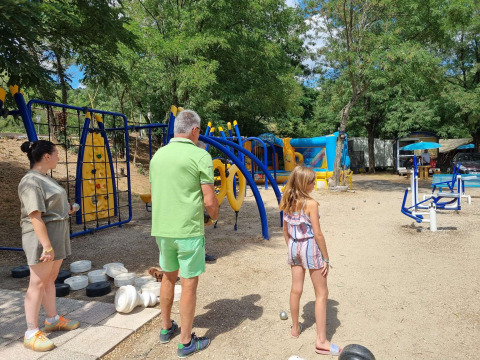 Familie spielt Boule neben einem farbenfrohen Spielplatz im Camping Paradis Family des Issoux, Frankreich.