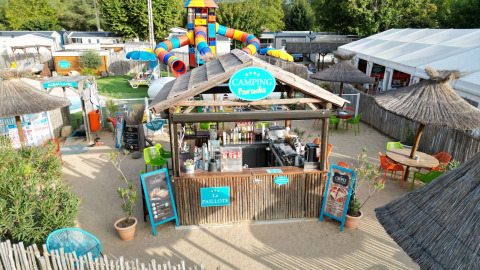 Camping Paradis Family des Issoux avec toboggans colorés, cabane de plage en bois et parasols de paille.