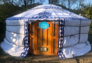 Et billede af en traditionel mongolsk jurte med dekorativ orange dør ved Camping Paradis i Auvergne-Rhône-Alpes.