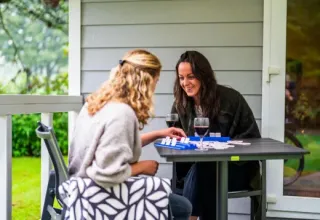 Two women playing a board game and enjoying wine on a porch at Holiday Park Latour in North Brabant.