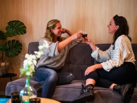 Dos mujeres brindan con vino en una sala acogedora del parque vacacional Latour en Brabante Septentrional.