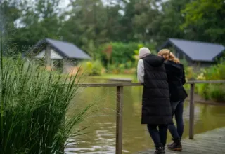 Due persone ammirano il lago al parco vacanze Latour nel Brabante Settentrionale, Paesi Bassi, circondate dal verde.