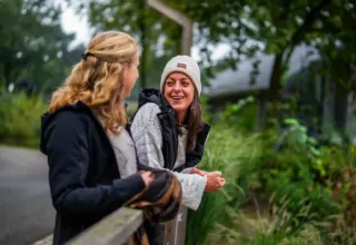 Two women chat and smile outdoors at Holiday Park Latour in North Brabant, Netherlands, among greenery.