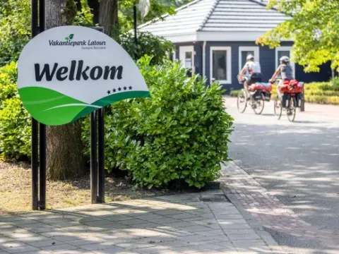 Cartel de bienvenida en el parque vacacional Latour en Brabante Septentrional, Países Bajos, con ciclistas al fondo.
