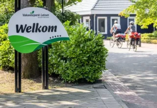 Cartel de bienvenida en el parque vacacional Latour en Brabante Septentrional, Países Bajos, con ciclistas al fondo.