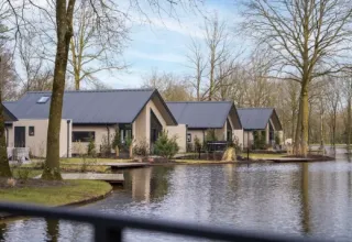 Holiday cottages next to a pond at Latour holiday park in North Brabant, Netherlands, among trees.