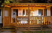 Cabaña SunLodge iluminada con porche de madera y cartel, ideal para unas vacaciones nocturnas acogedoras.