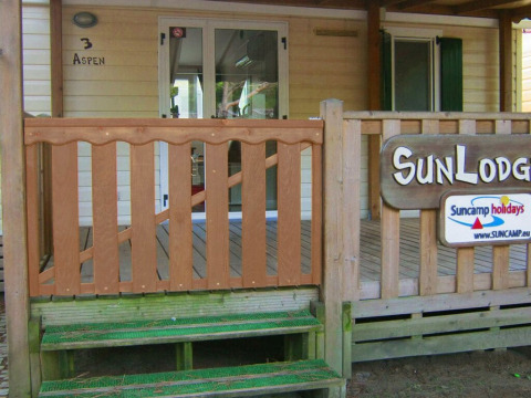 Entrada a SunLodge Aspen en Altomincio Family Park, Italia, con terraza de madera y escalones verdes.
