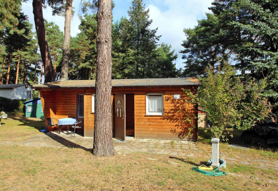 Knusse Bungalow 35 qm 2 Pers. tussen bomen, met tafel en stoelen buiten aan de voorkant.