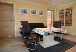 Woonkamer in lodge 'Am Strand' in Duitsland met moderne meubels, wanddecoratie en veel licht.