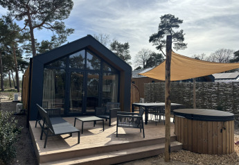 Boslodge accogliente con terrazza, sedute esterne, sauna e hot tub immersi in un ambiente boschivo.