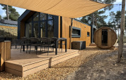 Outdoor deck of Boslodge with seating, hot tub, and round sauna, set amidst natural woodland surroundings.
