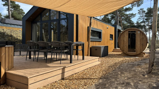 Outdoor deck of Boslodge with seating, hot tub, and round sauna, set amidst natural woodland surroundings.
