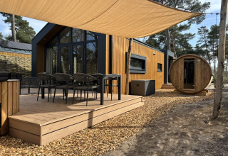 Udendørs terrasse ved Boslodge med siddepladser, hottub og en rund sauna omgivet af træer og natur.
