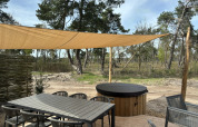 Outdoor deck at Boslodge with dining table, chairs, shade canopy and covered hot tub in a forest.