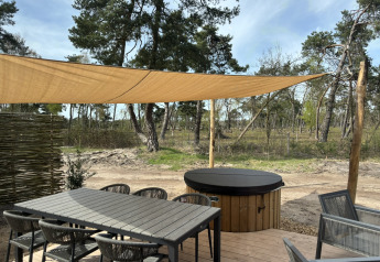 Terrazza con tavolo, sedie, tenda parasole e vasca idromassaggio coperta nella natura di Boslodge.