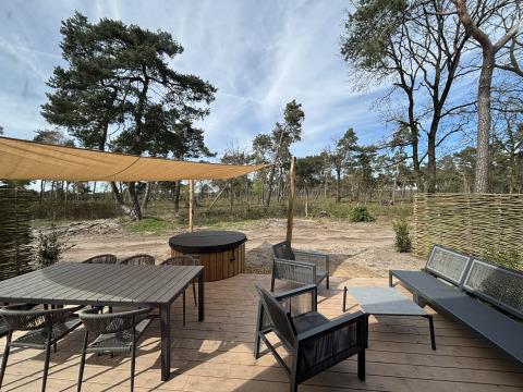 Terrasse en bois de Boslodge avec table, fauteuils, bain à remous et vue sur la forêt environnante.