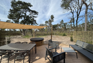 Træterrasse ved Boslodge med spisebord, loungemøbler, hottub og naturudsigt til skovområde.