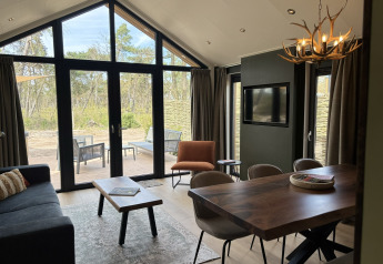 Soggiorno di tiny house moderno con ampie finestre, tavolo da pranzo, divano e vista sulla terrazza esterna.